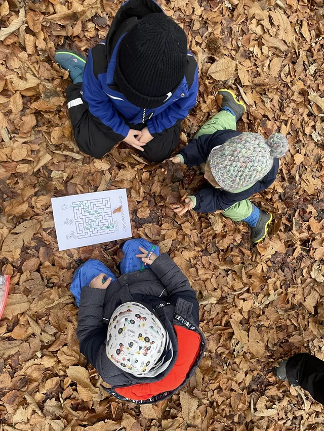 Kinder suchen bei einer Schnitzeljagd-Station im Herbstlaub